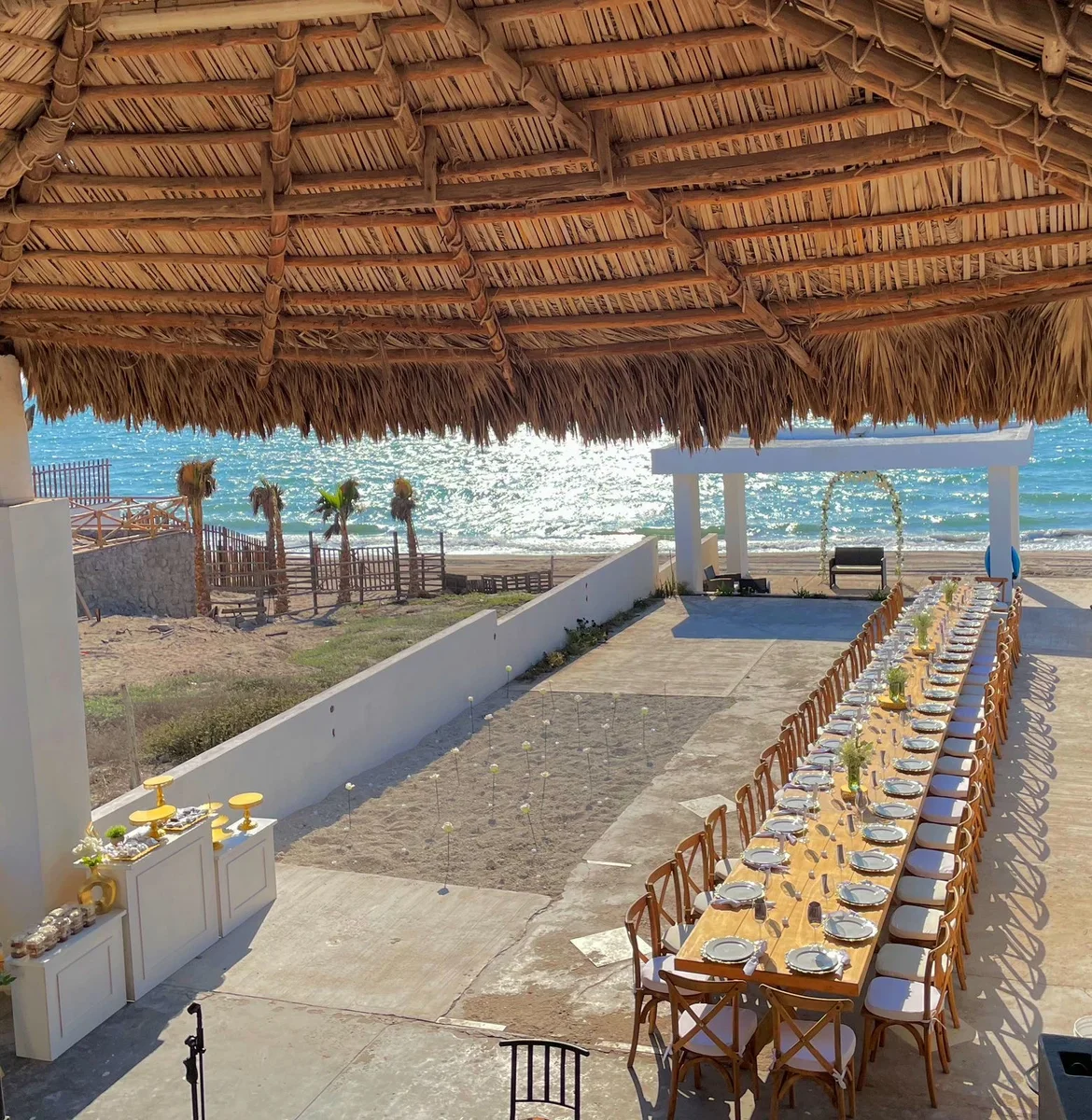 Mesa imperial en playa bajo palapa con sillas Crossback
